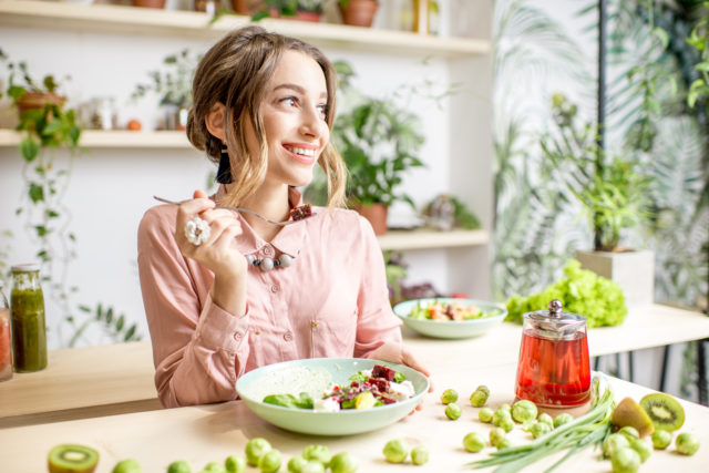 Young woman sitting with healthy food in the beautiful interior with green flowers on the background