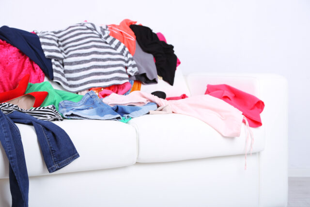 Messy colorful clothing on white sofa on white wall background - clothes made of synthetic fibers and containing microplastics