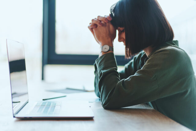 Side view of exhausted upset businesswoman having difficulty concentrating, seeking a solution using laptop while sitting in office in front of the window. Empty space