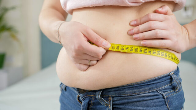 Closeup of overweight woman using measuring tape. Concept of dieting, unhealthy lifestyle, overweight and obesity SSUCv3H4sIAAAAAAAACnyRy27DIBBF95X6DxbrWPULx8kXdFOp+6gLDBMbBUMEOFUV5d87GDti0+6Yc+fBnbm/vmQZ6ZmTnByze4gwlkrNzlvmpdGIi93KLWgBNiU3W7dFCkBIb6xkKoU983zUbAKEelYq4MciEueZnx24MH1FnHkYsEeEzxbxi6cYZ5uwiFiBEvkEc1VAdoni5j4oZENxxB/178CUHzmz8PaBPjia+LdXfHxtLtkAmv8sRhKDFhSwaPAUU8nl24OdUstsFtIkbm8Gh4eEOul0tZJLPSRlxo/LOZ6bw6uZKQHa+GUyiUaIwNWGsKyr9tDs67otm4oW+65cE+I5Rol9bLSyccMvUqR/liJ0OleU06Jrc9oJkTfNuc37ipb5oYei35e8Eg3FjT1+AQAA//8DAPwSl9ZpAgAA