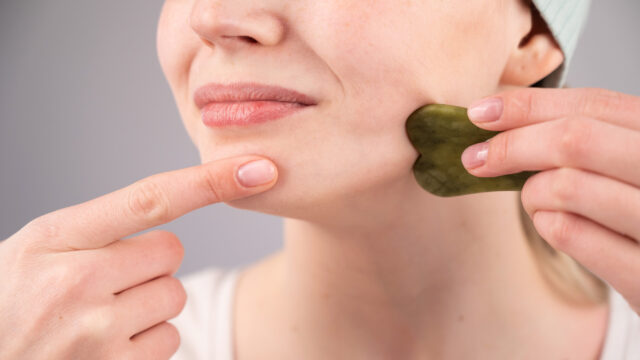 Close-up portrait of a young woman massaging her face with a gouache scraper